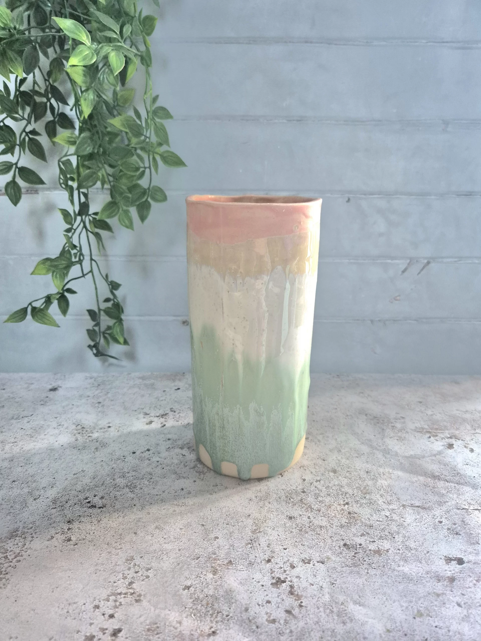 A large ceramic tall vase crafted from white stoneware clay and finished in layered glaze with pinks, greens and white tones.


