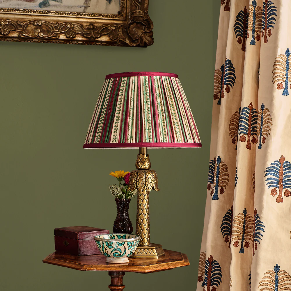Penny Morrison Taara stripe pleated silk lampshade in red and blue with a decorative red trim, showcasing a traditional English country house lighting aesthetic.
