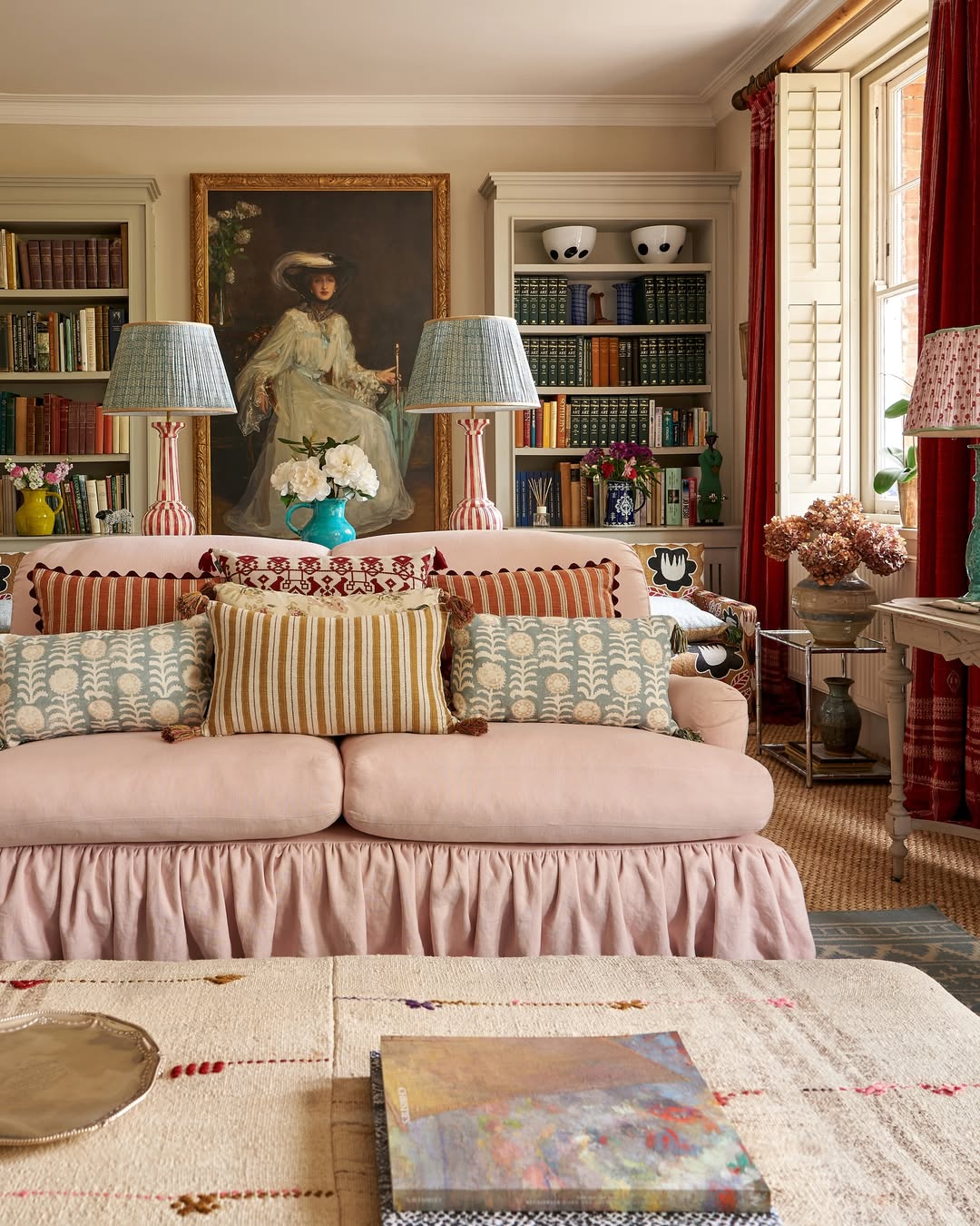 English country house library featuring a pink skirted sofa, floor-to-ceiling bookshelves, and a curated gallery wall with an antique portrait.