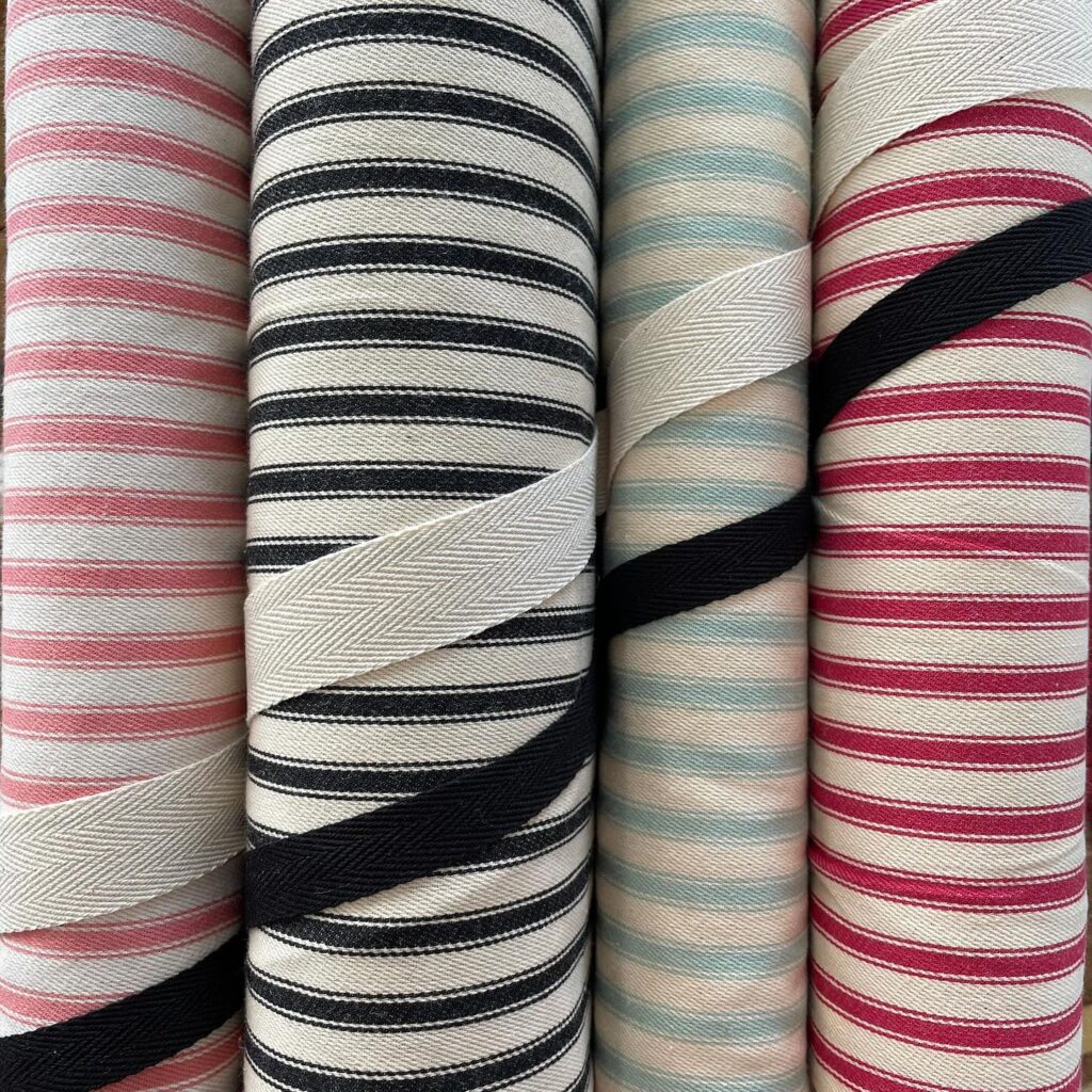 Striped ticking fabric in pink, black, duck egg blue and red on a cream background